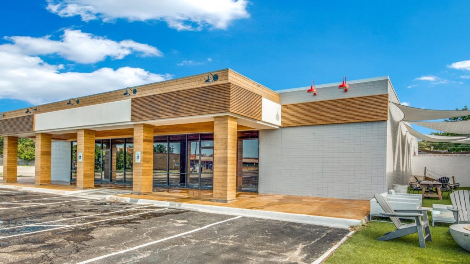 Storefront with wood accents, large windows, and a small outdoor seating area under a white canopy. Blue sky.