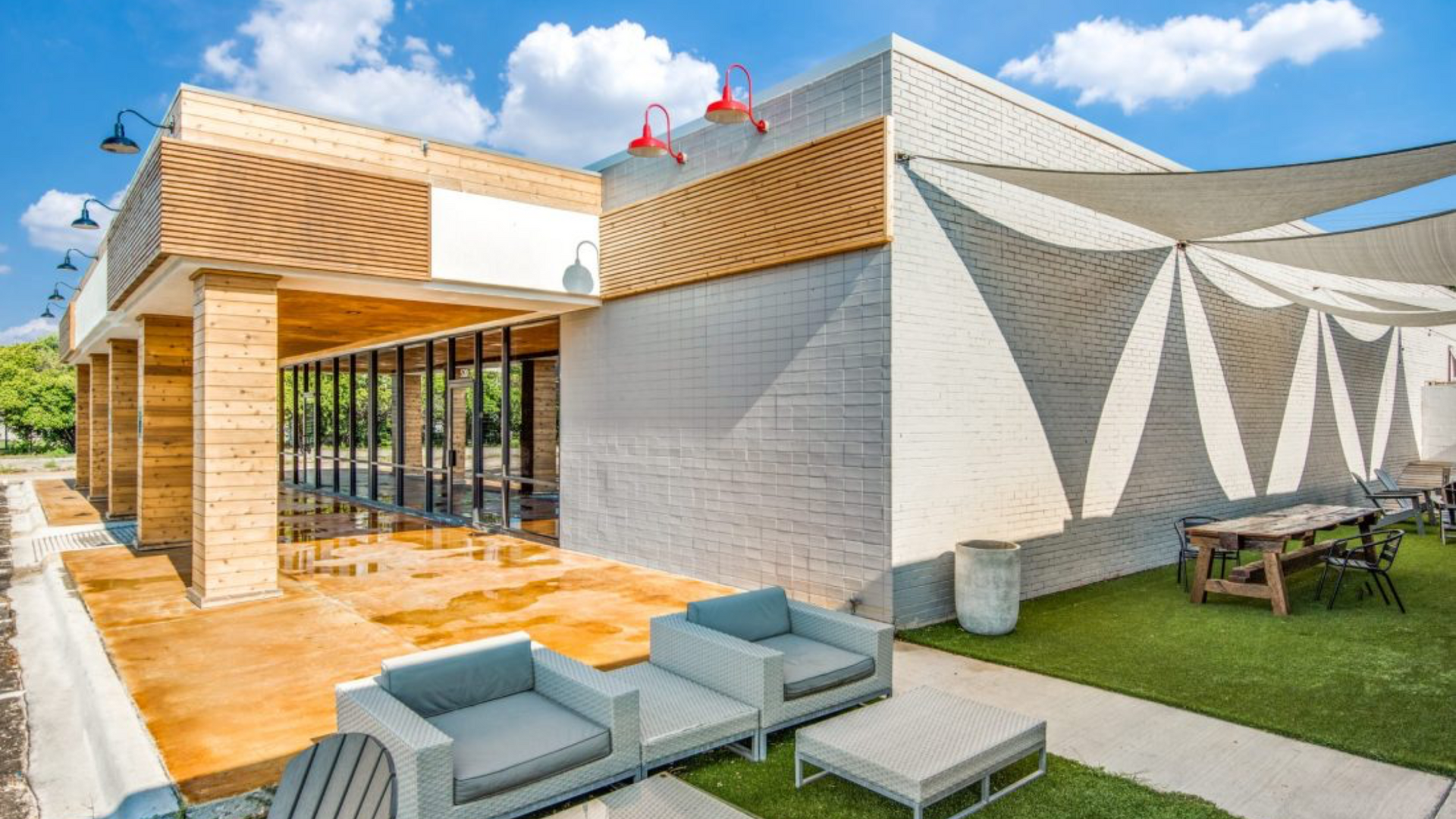 Modern brick building with patio, tables, and chairs under a shaded canopy.
