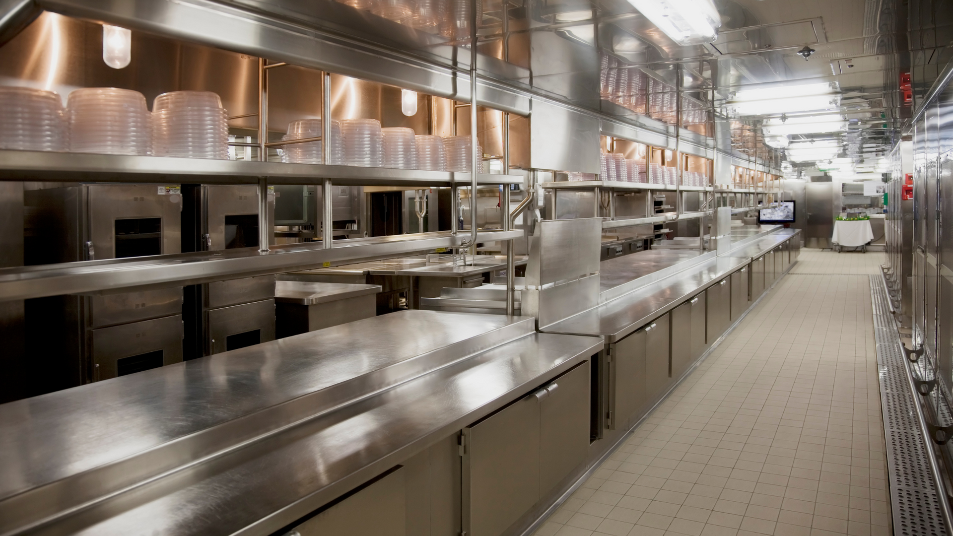 Long, stainless steel commercial kitchen with shelves of plastic containers and work surfaces.