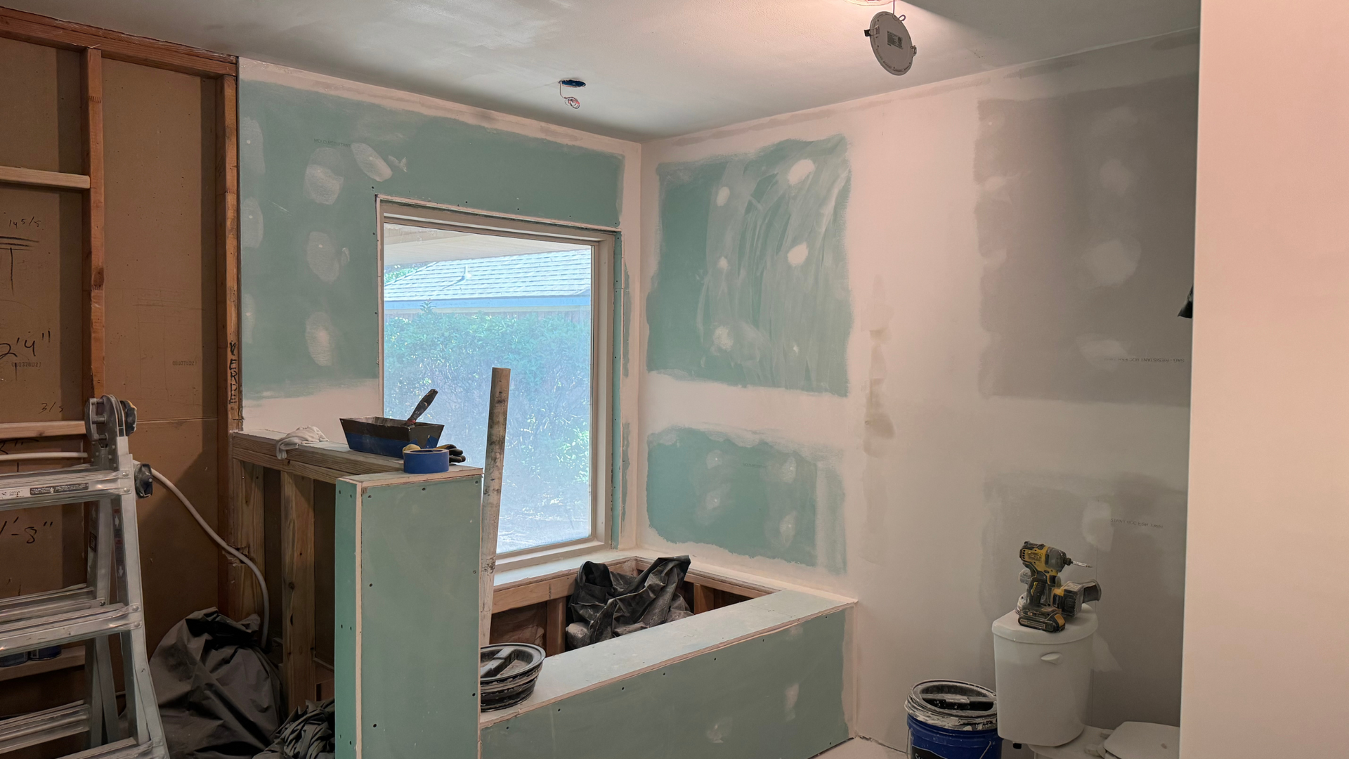 Bathroom renovation with exposed studs, new drywall, and a window.