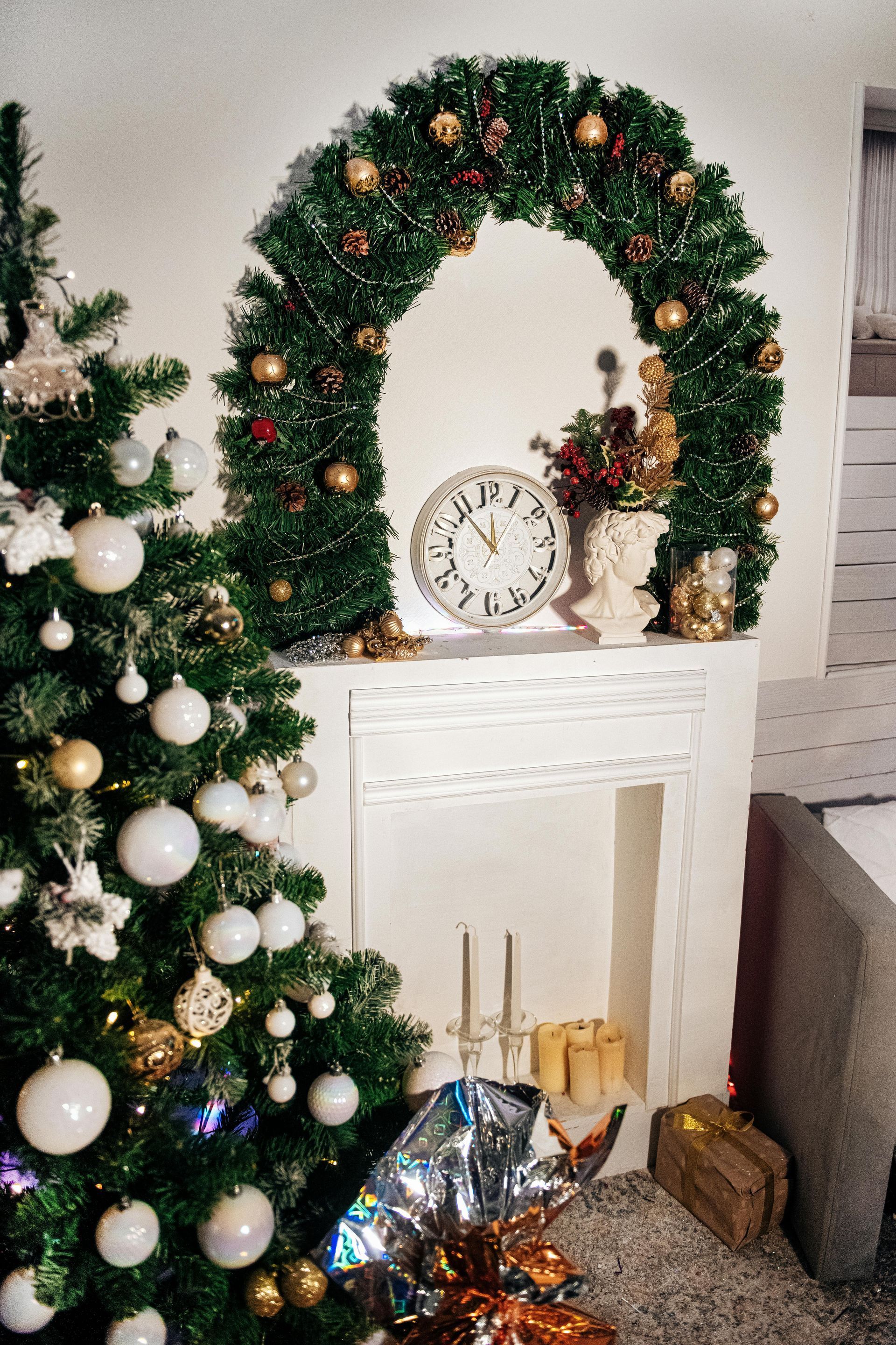 A christmas tree is sitting next to a fireplace decorated with a wreath and a clock.