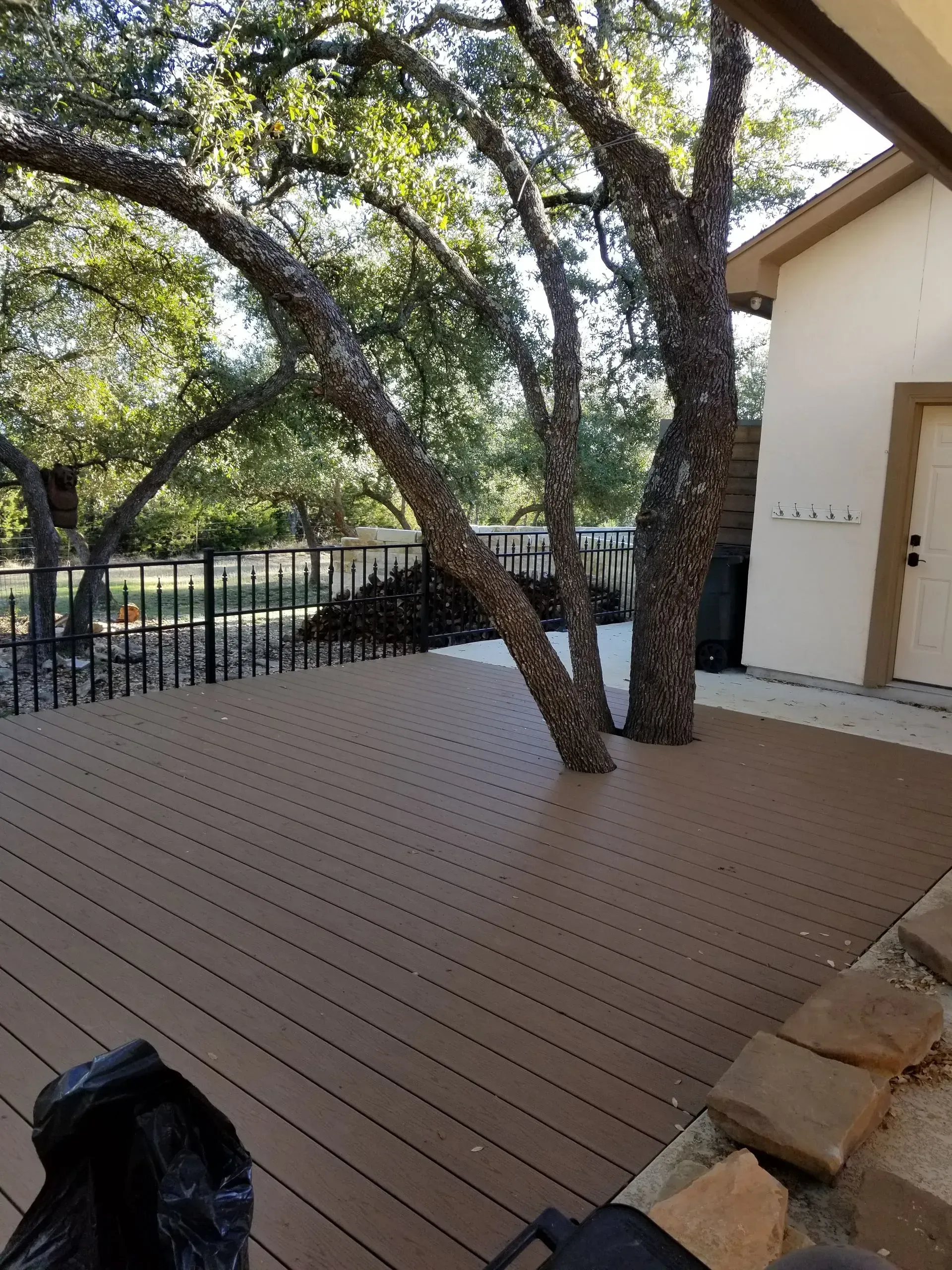 Brown composite deck with trees growing through it, next to a beige building.