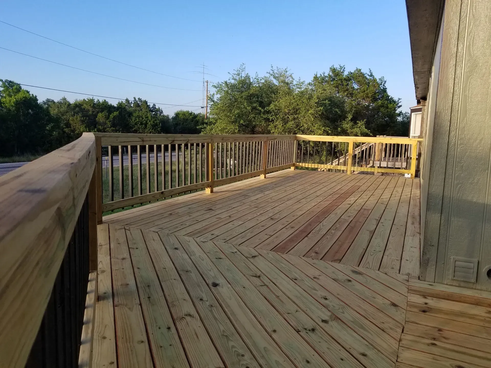 Wooden deck with railing, trees in the background, blue sky.