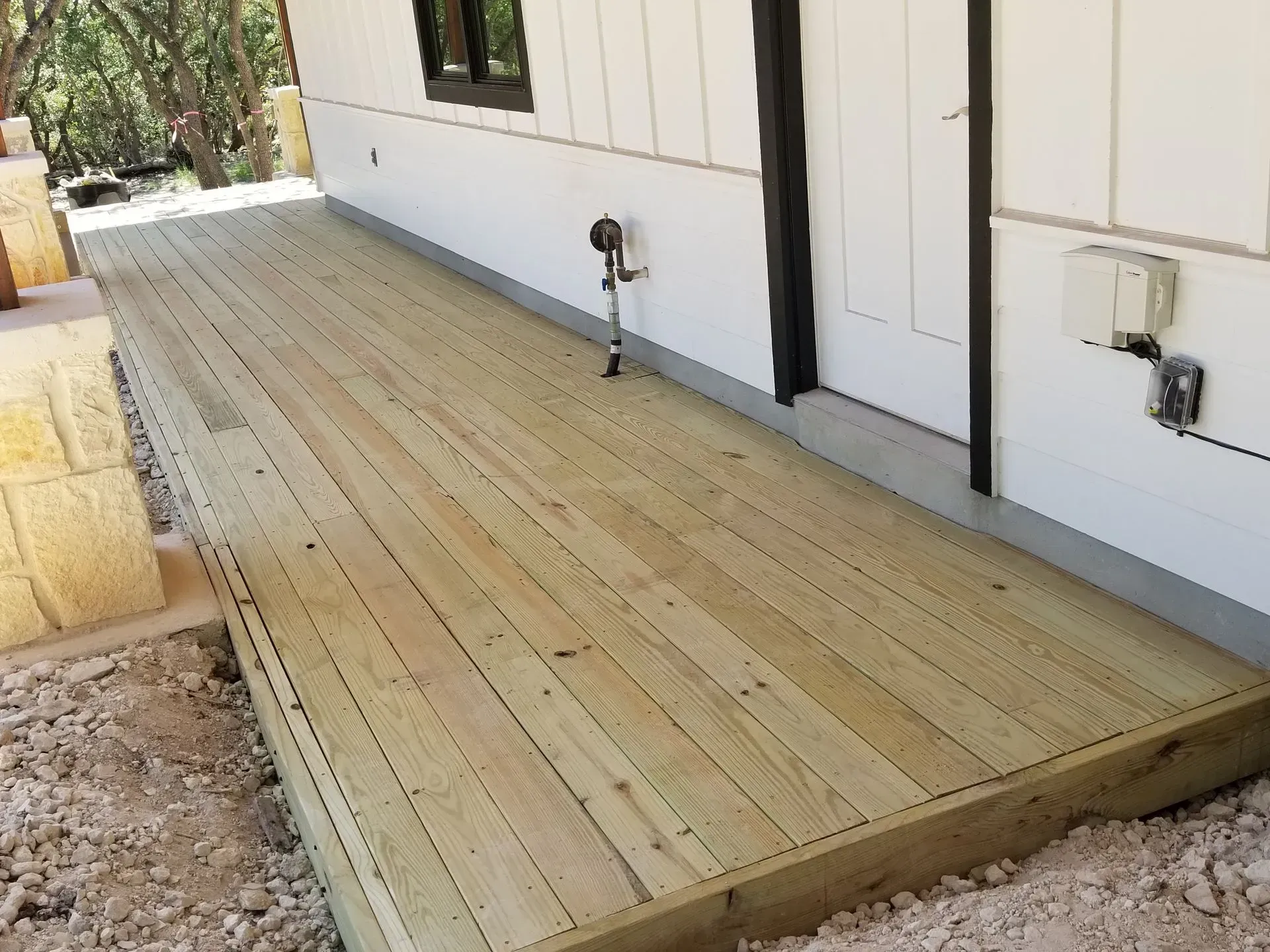 Wooden deck extending from a white house with black trim. Outdoor setting, ground visible.