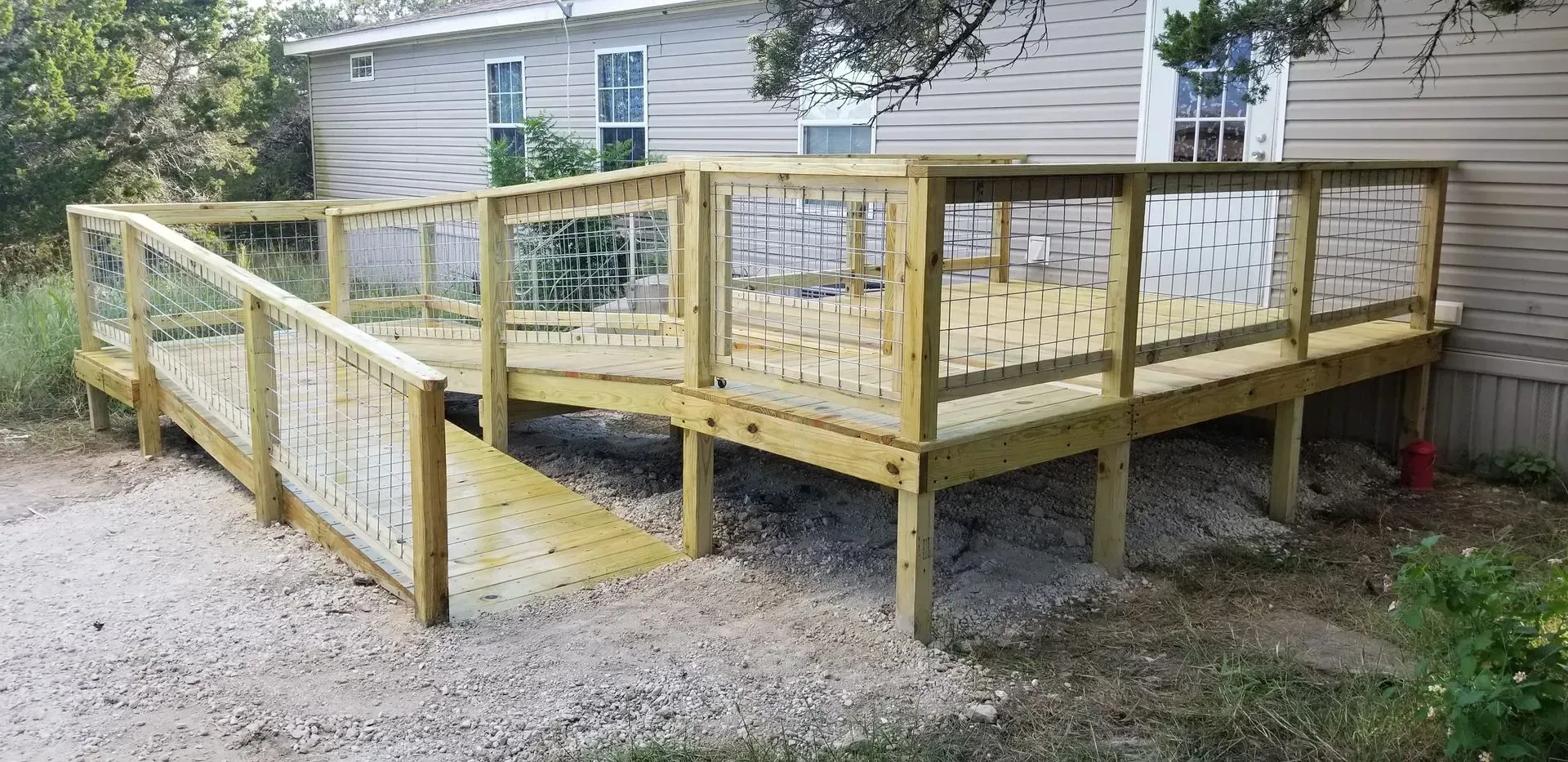 Wooden deck and ramp for accessibility, attached to a house with gravel ground.