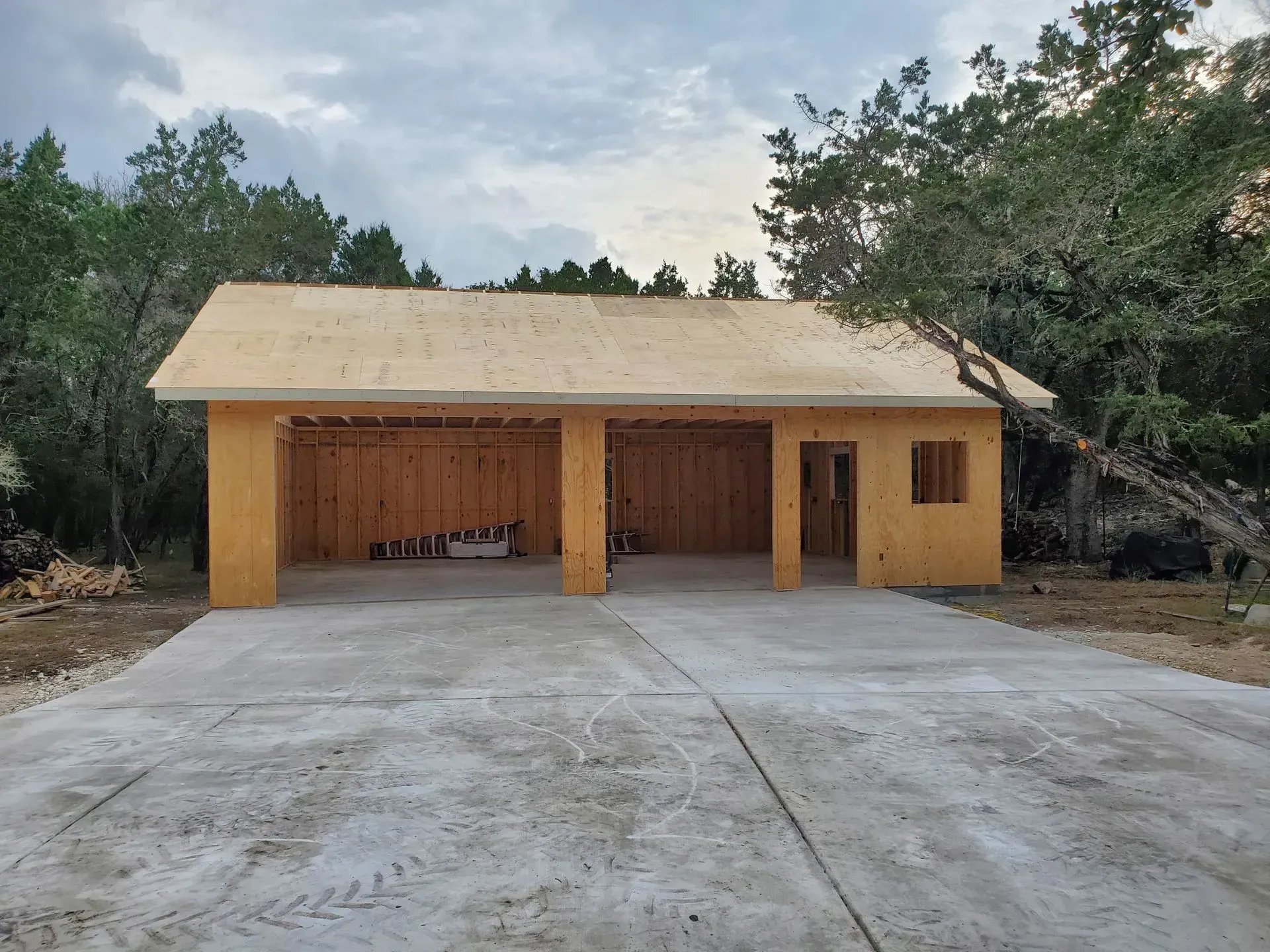 Newly constructed wooden garage with two bays, set on a concrete slab in a wooded area.