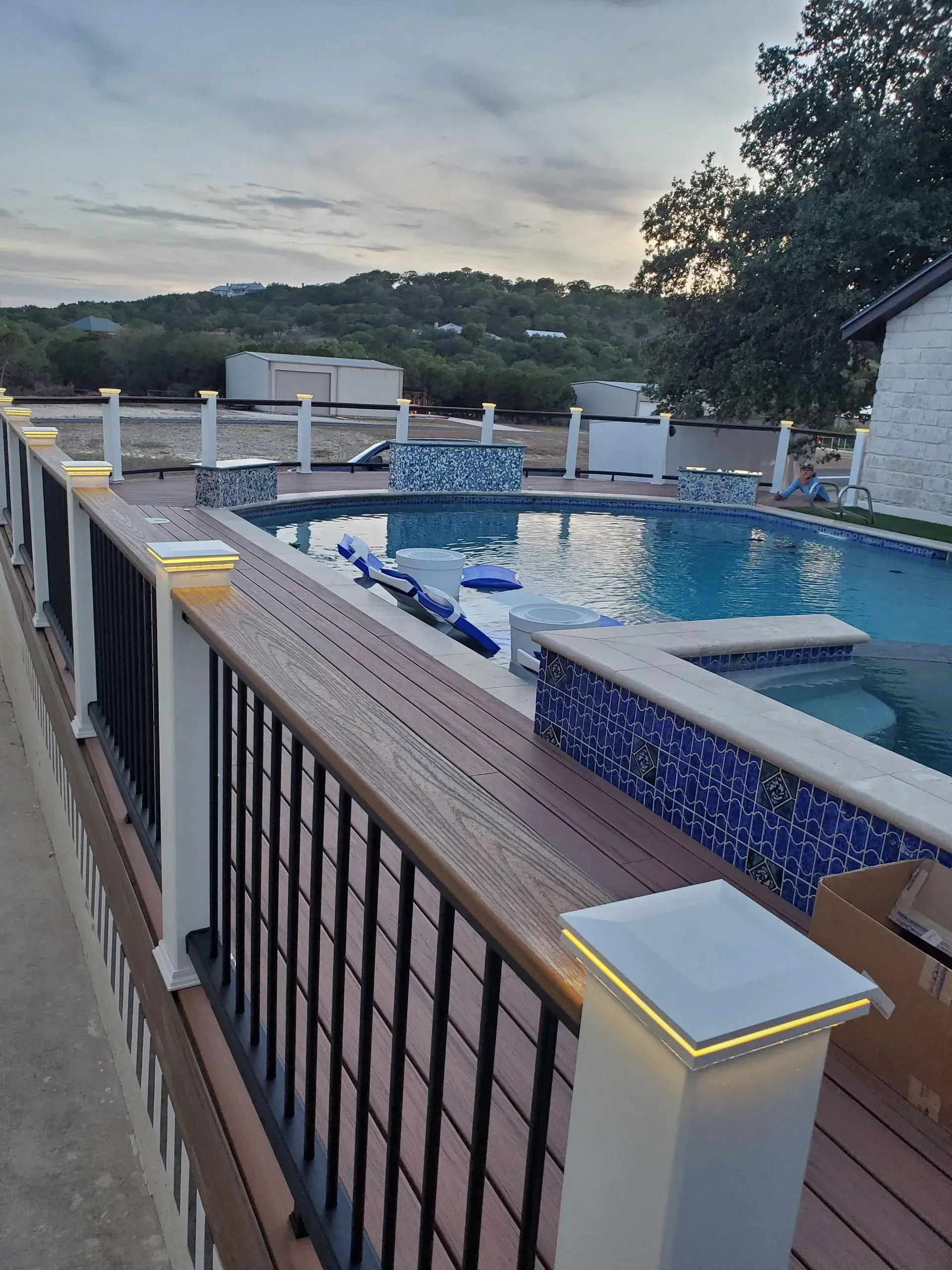 Pool deck with a swimming pool, spa, and decorative lights. The deck has brown composite boards and black railing