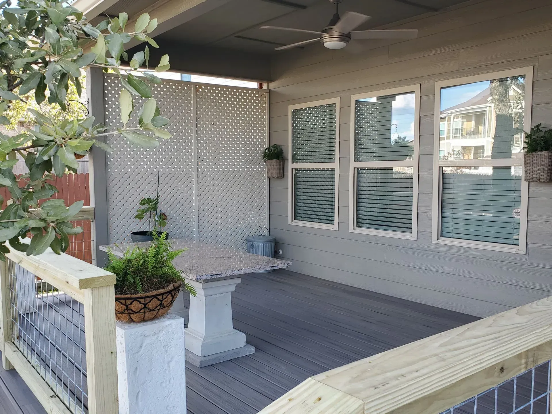 Covered deck with a light grey floor, table, and windows. A decorative screen and foliage are visible.