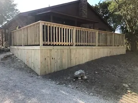 Wooden deck built around a cabin with a sloped gravel yard.