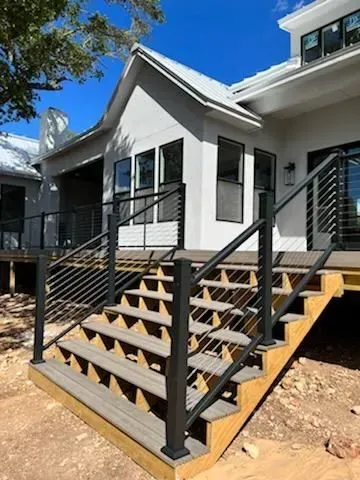 Wooden outdoor staircase with black metal railings leading to a white house with windows.