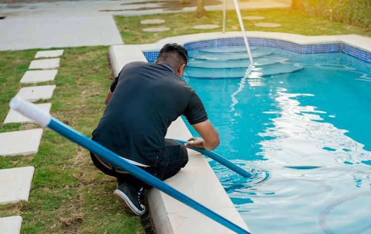 Person cleaning a backyard pool with a blue vacuum hose