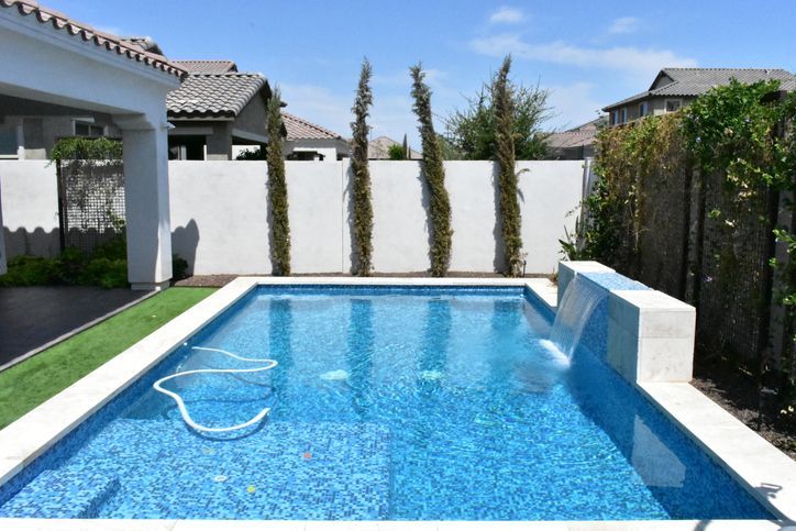 Backyard swimming pool with bright blue water, white walls, and a pool cleaner hose