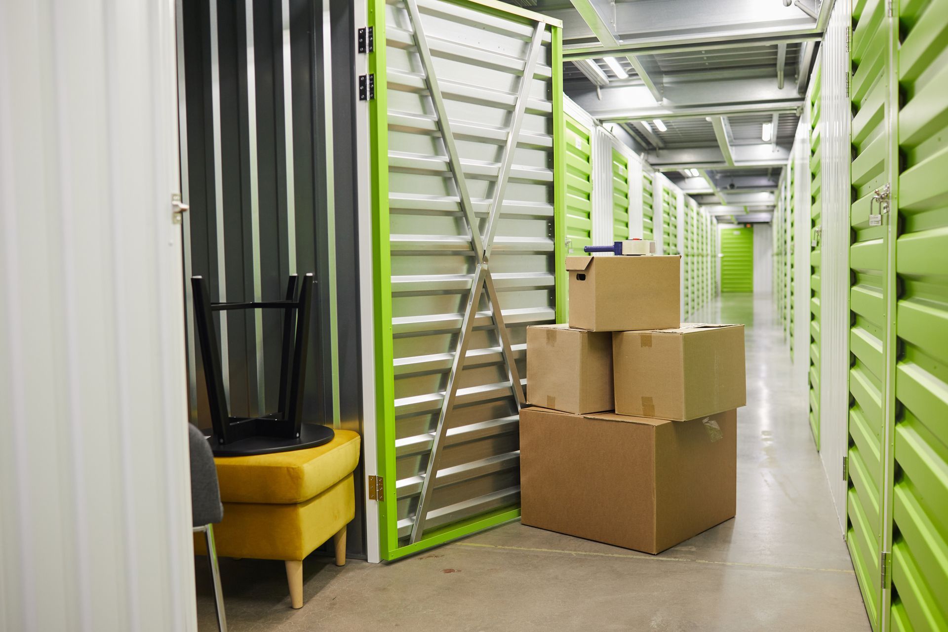 Storage units, a hallway with open green doors, cardboard boxes, and a stool.