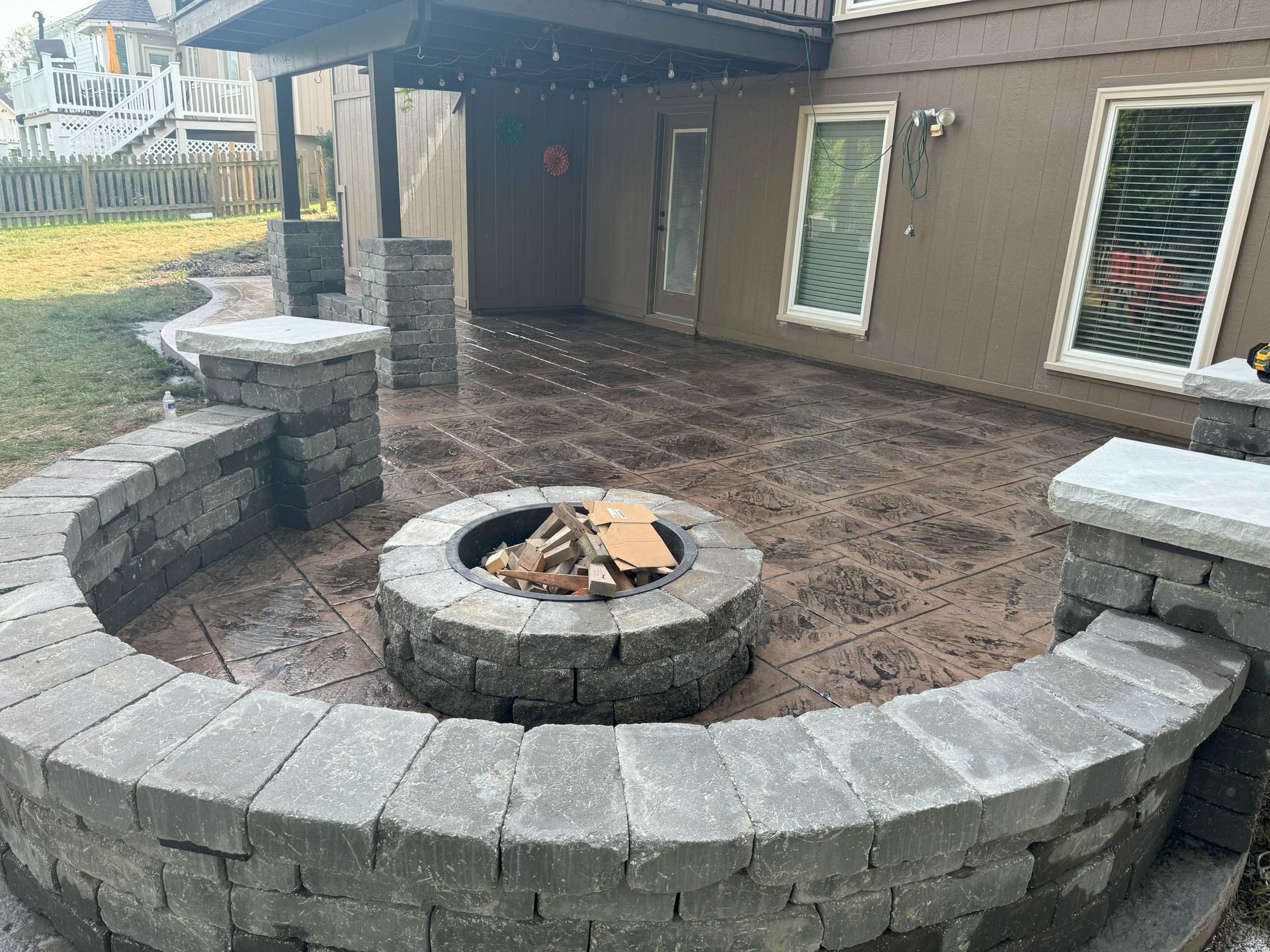 Backyard Patio With Fire Pit, Tables, Chairs, Pink Flowers, And Black Mulch Landscaping.