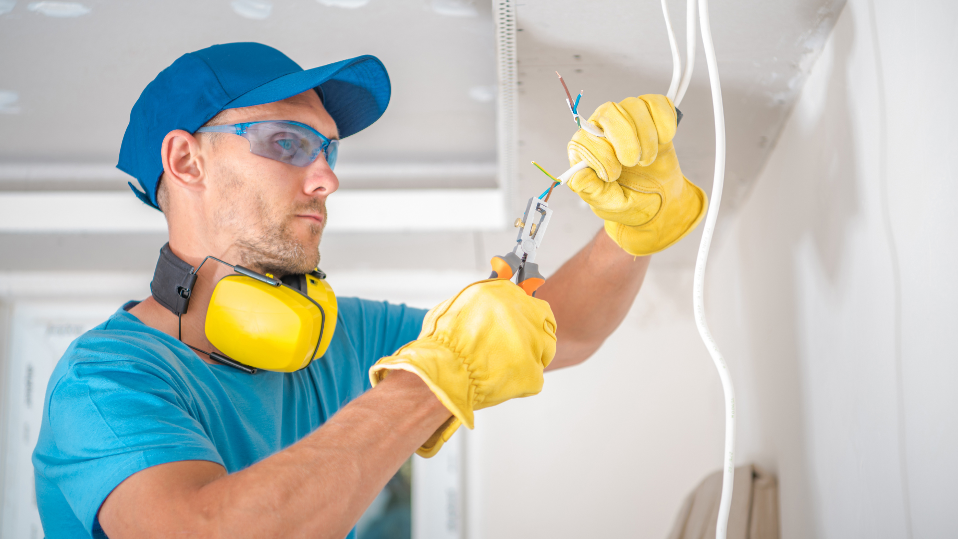 A man wearing ear muffs and safety glasses is working on a light fixture.