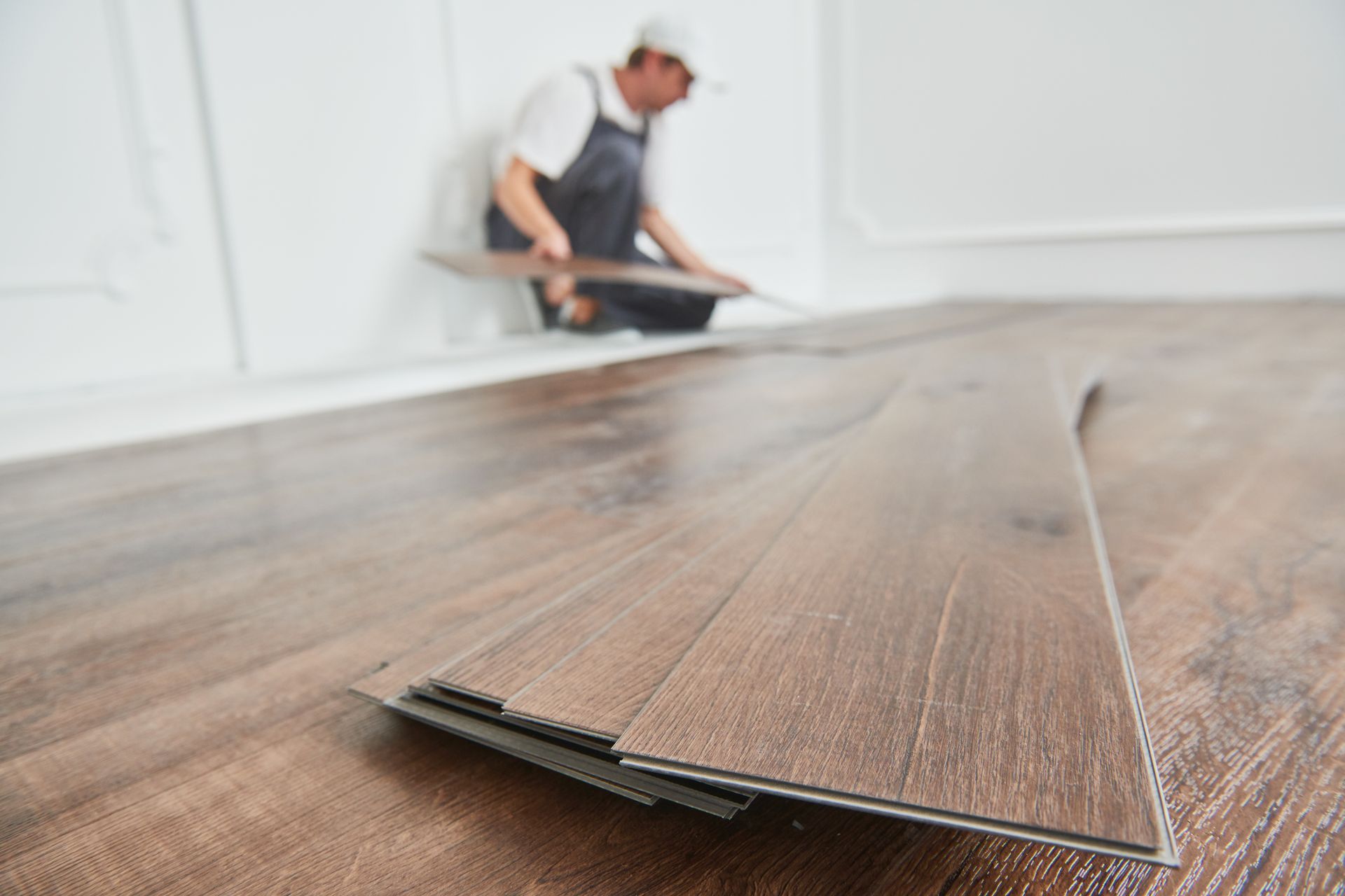 Person wearing gloves installing light wood laminate flooring.