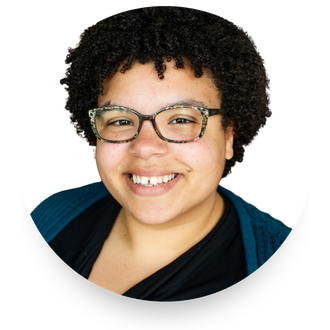 Smiling woman with glasses and short curly hair, wearing a blue top against a white background.