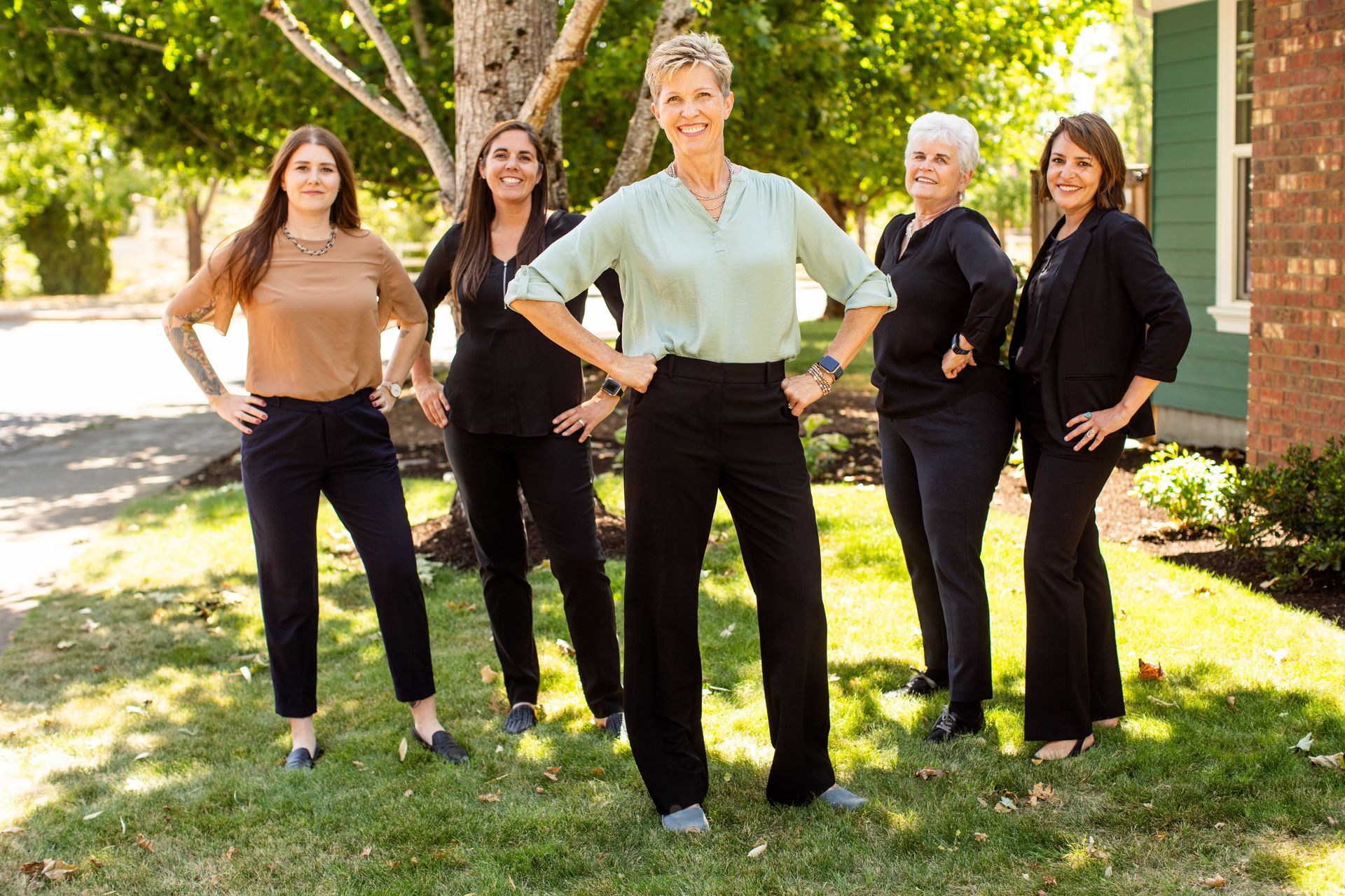 Five professional women standing in a yard, hands on hips, smiling.