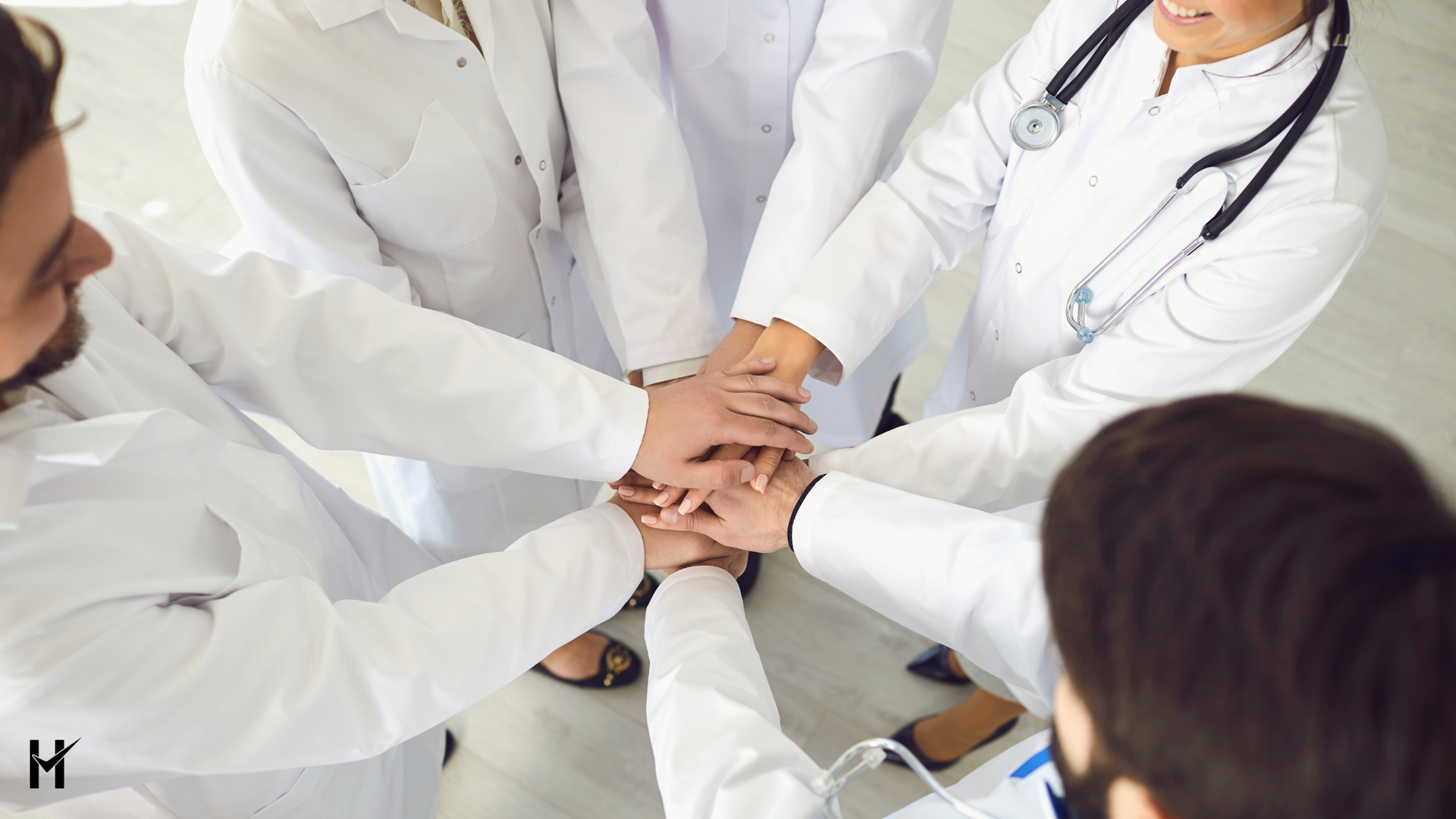 Medical team in white coats with hands stacked together.