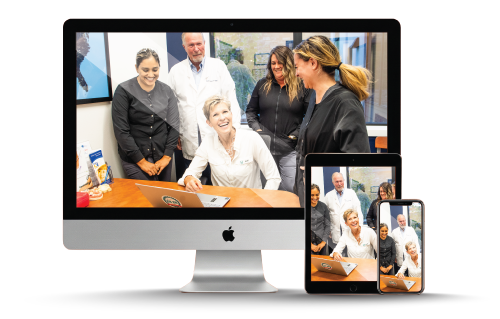 Team gathered around a desk, looking at a laptop on a large computer, tablet, and phone screen.