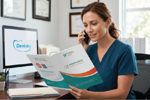 Woman on phone reading a brochure at a desk with a computer displaying a dental logo.