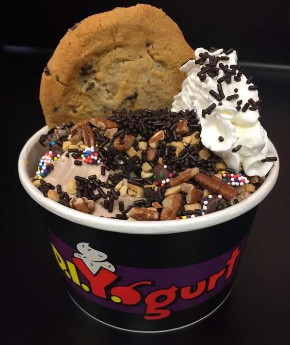 Frozen yogurt cup topped with cookie, whipped cream, chocolate sprinkles, and nuts