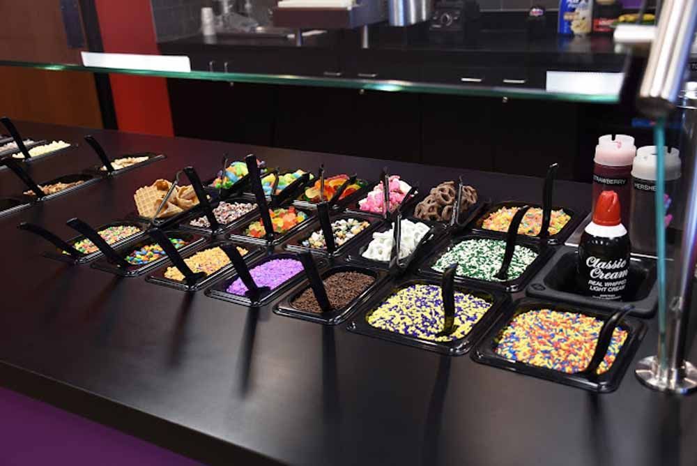 Assorted colorful candies in black trays on a counter, with a squeeze bottle on the right.