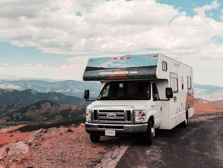 White RV parked on a mountain road with cloudy sky and scenic valley views