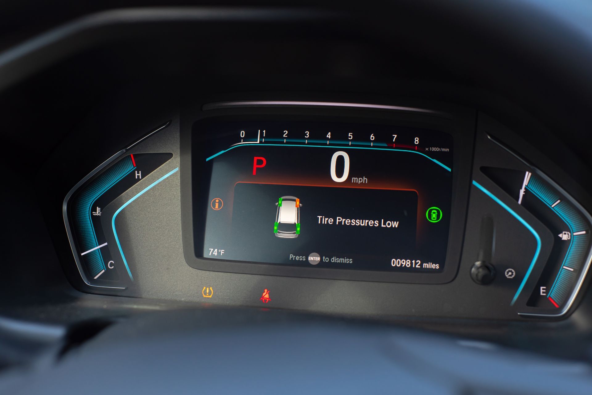 Car dashboard digital display showing speed 0, gear P, and battery status gauges glowing in blue and red.