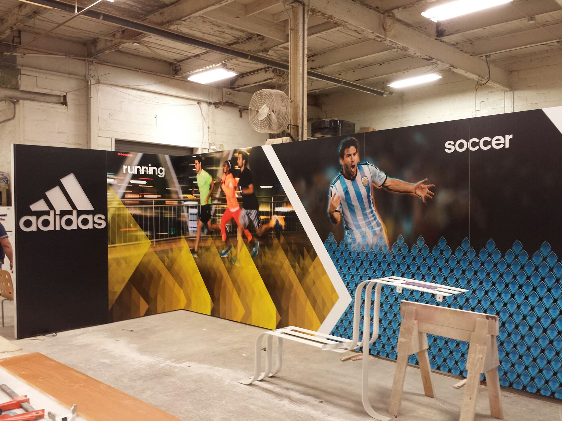 An Adidas display featuring a running section with yellow graphics and a soccer section with a player in a blue jersey.