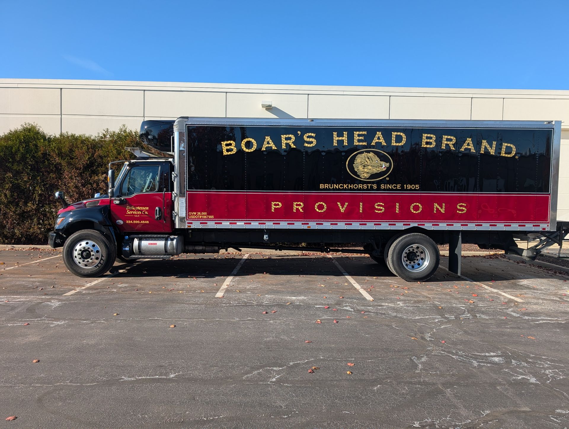 A Boar's Head Brand refrigerated delivery truck parked in a sunny, paved lot against a white building.