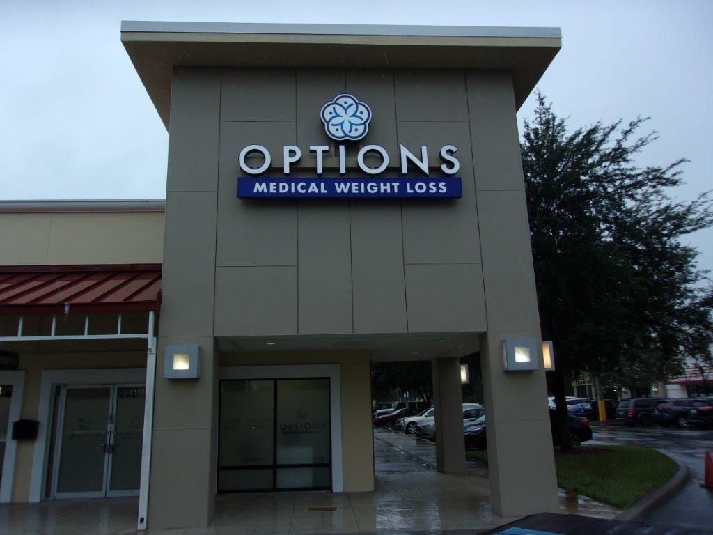 The exterior entrance of an Options Medical Weight Loss clinic, featuring a beige building facade and lighted signage.