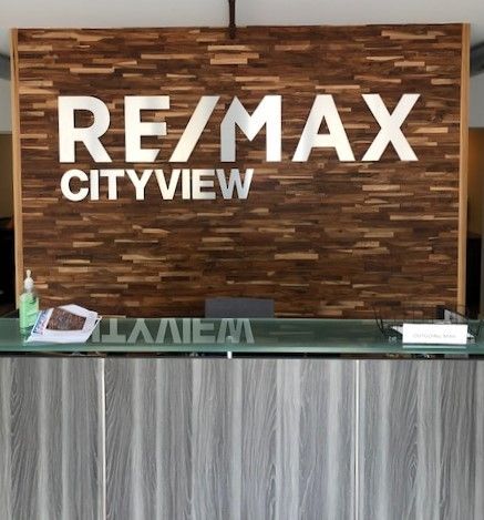 A RE/MAX Cityview reception desk with silver metallic logo letters against a textured, dark wood-paneled wall.