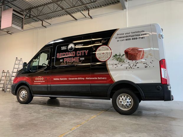 A black and white delivery van for Second City Prime featuring a logo, QR code, and an image of a steak on its side.