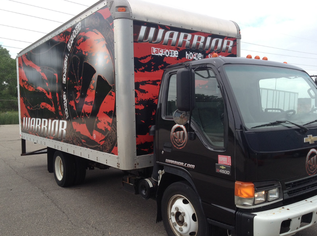 A black box truck parked on asphalt, featuring a red and black graphic wrap with the word 