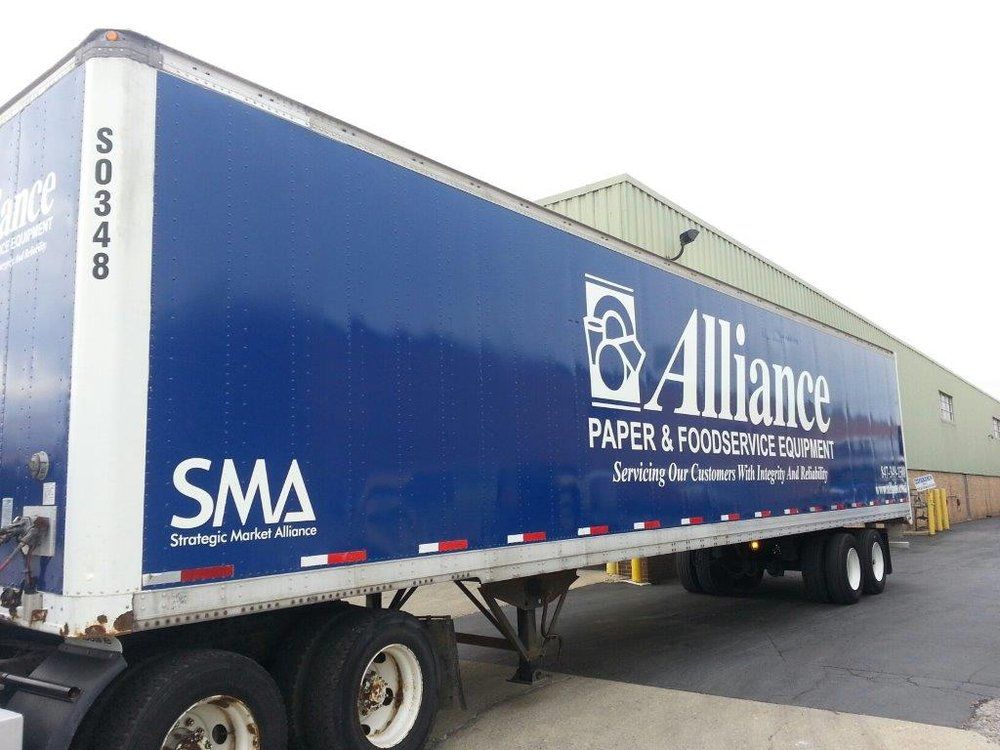 Large blue truck trailer featuring 'Alliance Paper & Foodservice Equipment' branding parked outside a warehouse, promoting customized vehicle wraps and fleet graphics in Chicago.