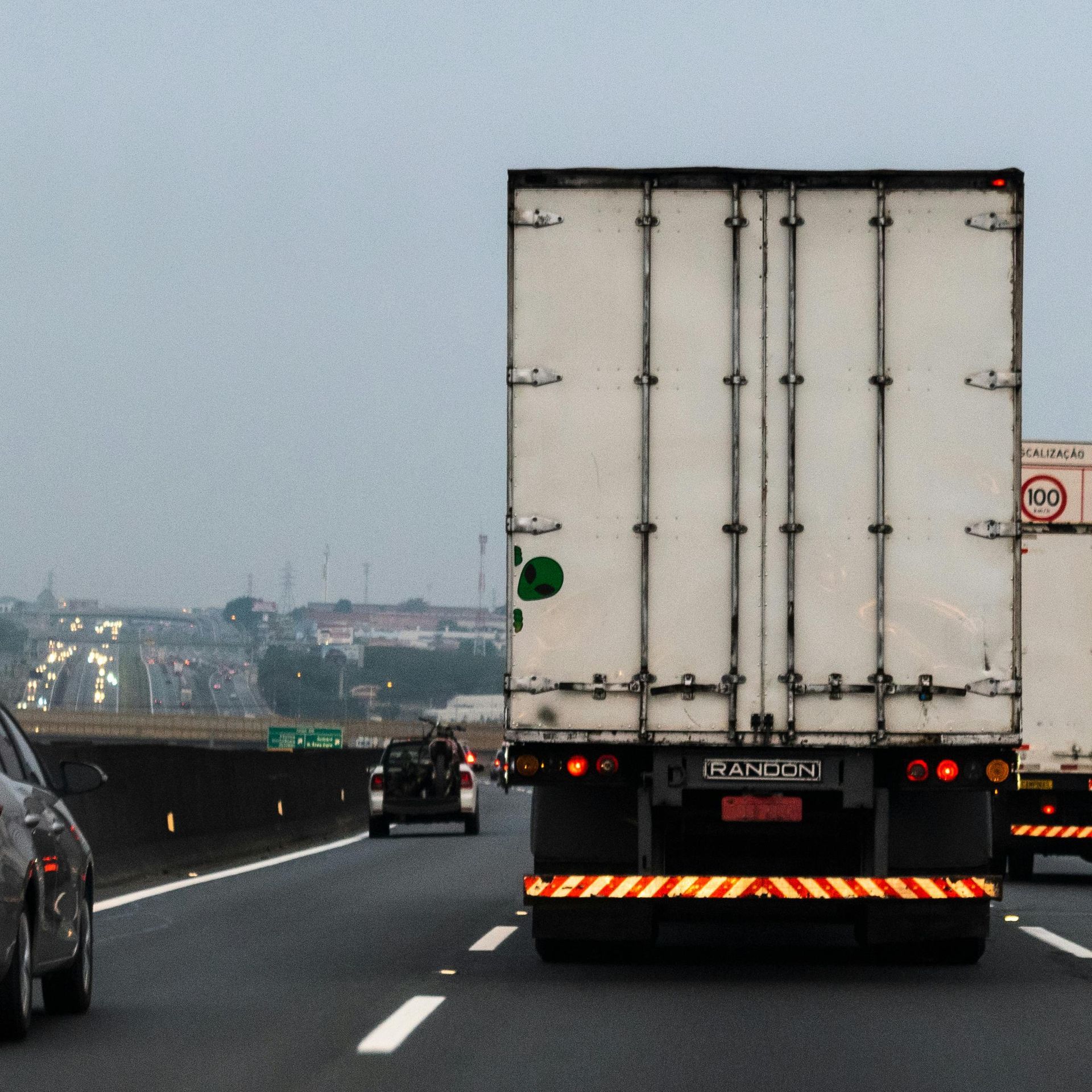 A white semi-truck travels on a highway during the day, with other vehicles visible nearby.