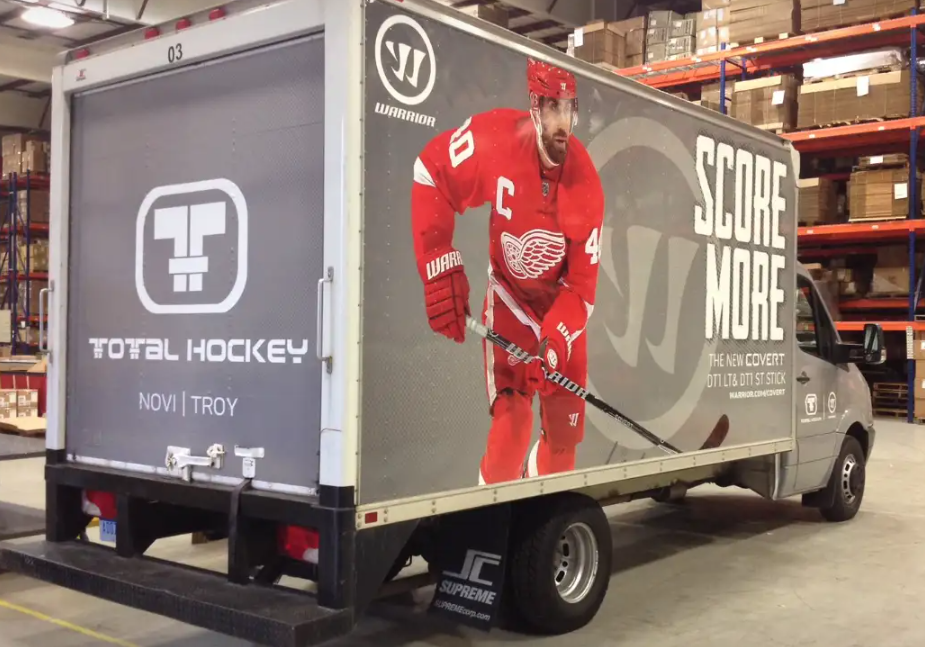 A Total Hockey delivery truck parked indoors, featuring a large image of a red-uniformed hockey player and
