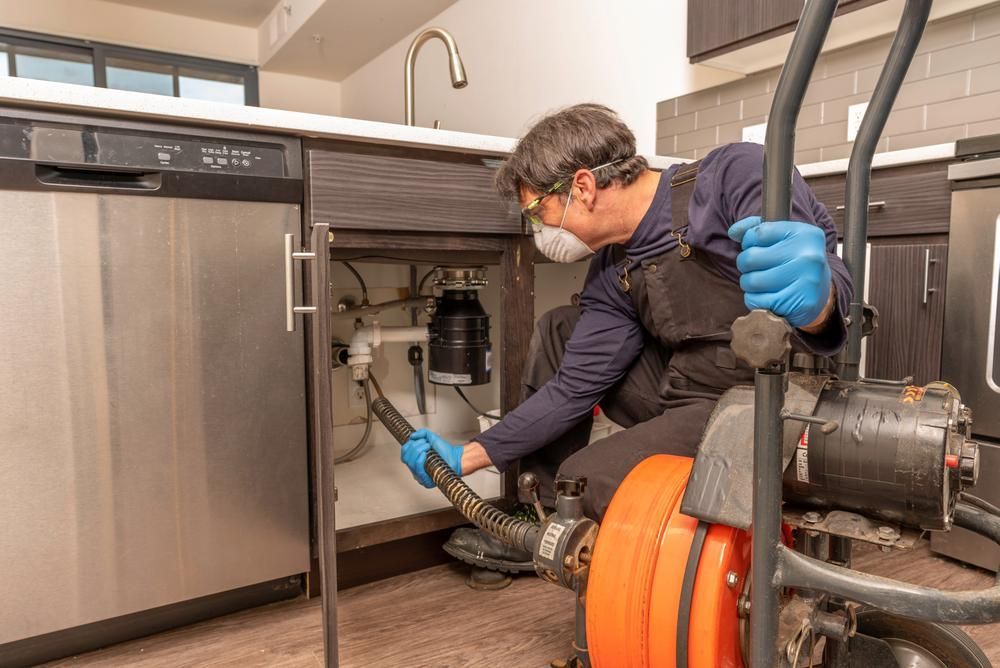 A Plumber Is Using A Machine To Drain A Sink In A Kitchen — Ashley Chick Plumbing In Baranduda, VIC