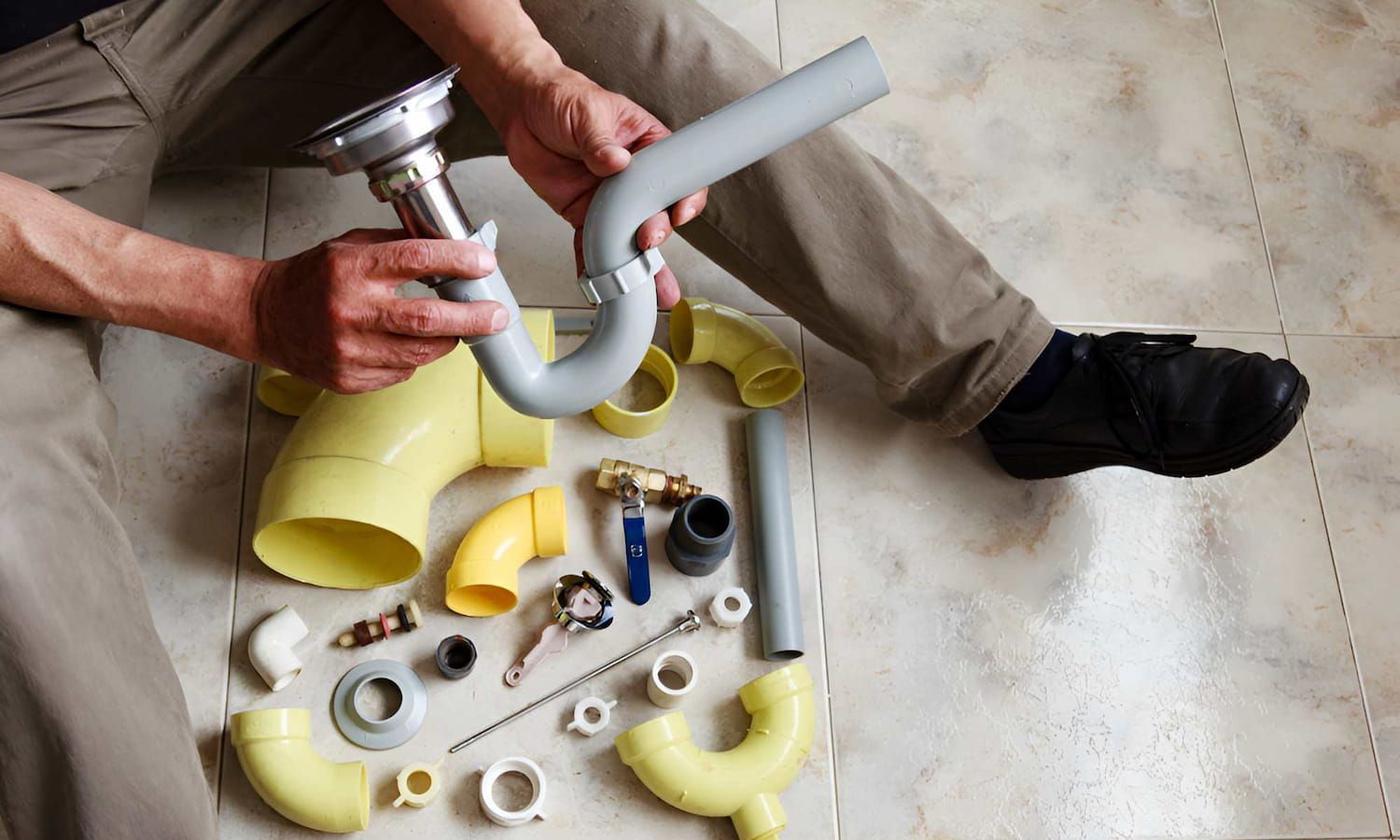 A Man Is Sitting On The Floor Fixing A Sink Pipe — Ashley Chick Plumbing In Baranduda, VIC