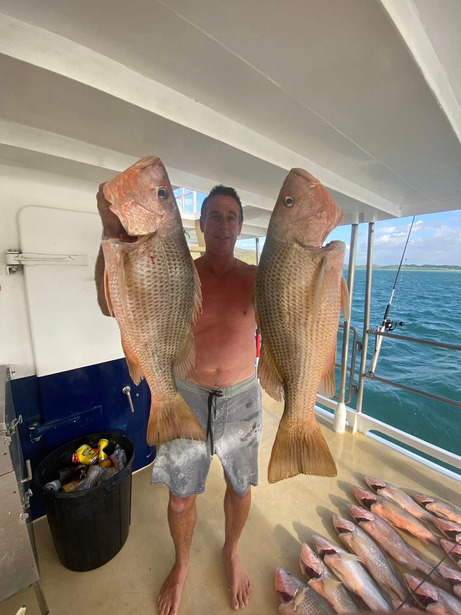 A person standing on a boat deck holding two large, textured reddish-brown fish, with more fish laid out on the floor.