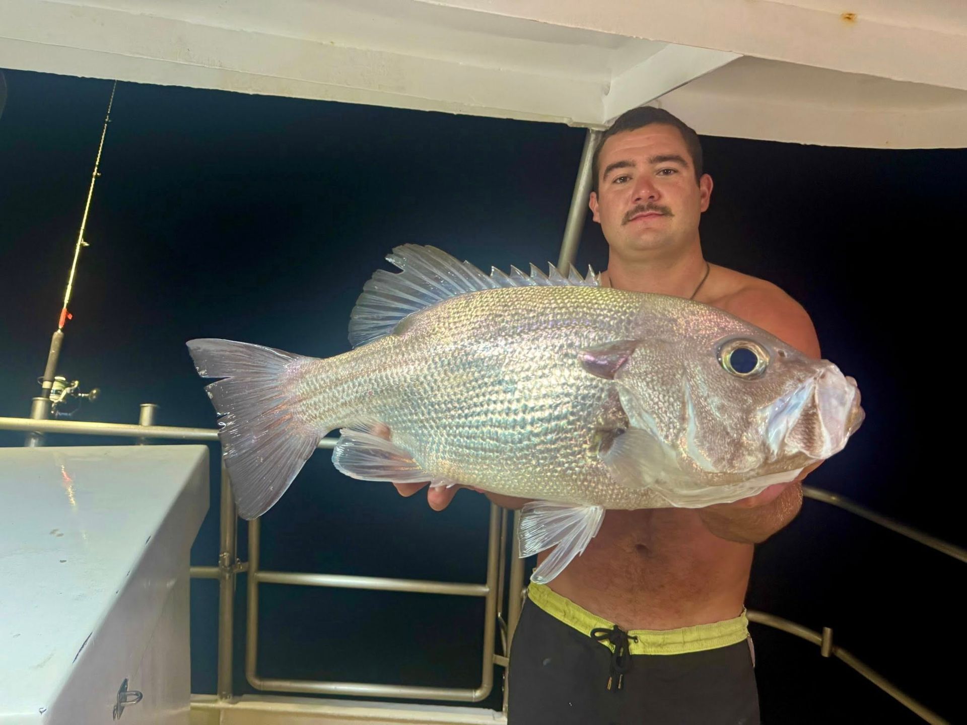 A person holding a large, silvery fish on the deck of a boat at night.
