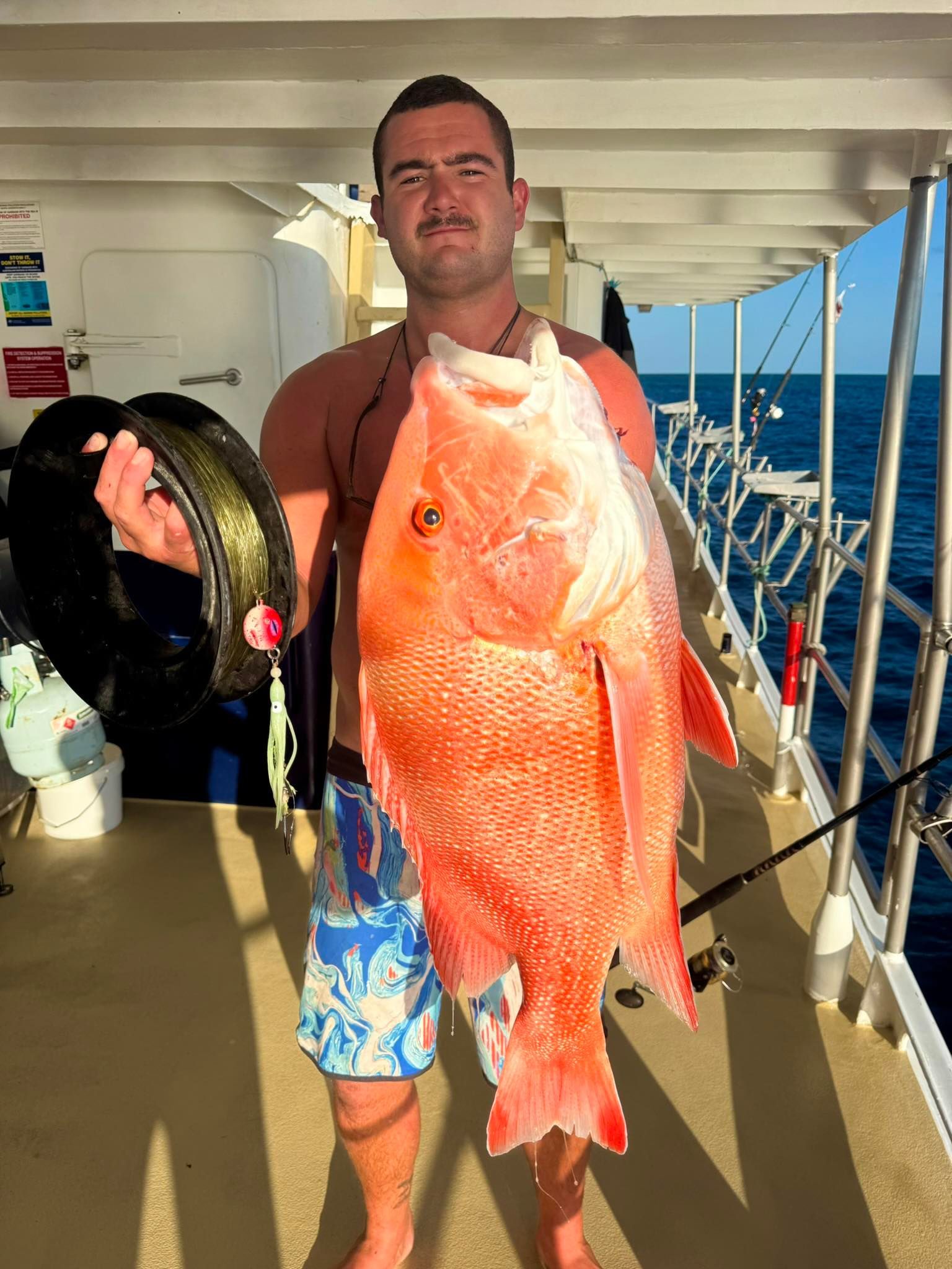 A person stands on a boat deck holding a large, bright orange fish.