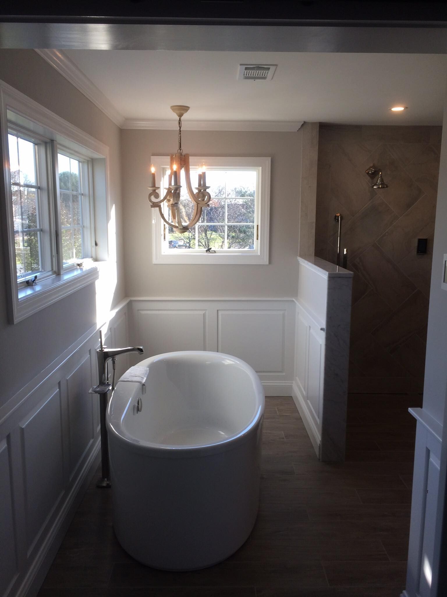Small bathroom with a white soaking tub, chandelier, window, and gray tiled shower area