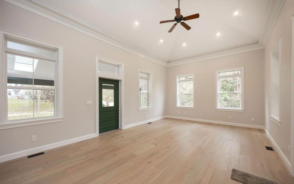 Bright empty living room with white walls, wood floors, green front door, and ceiling fan