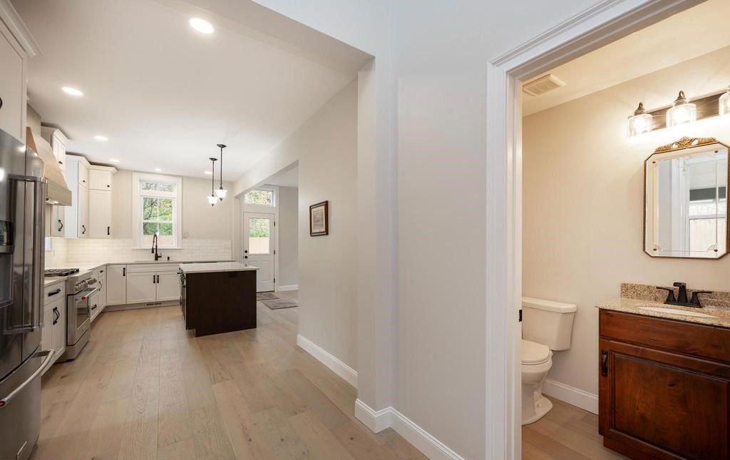 Bright kitchen with island and stainless appliances, opening to a small bathroom with wood vanity.