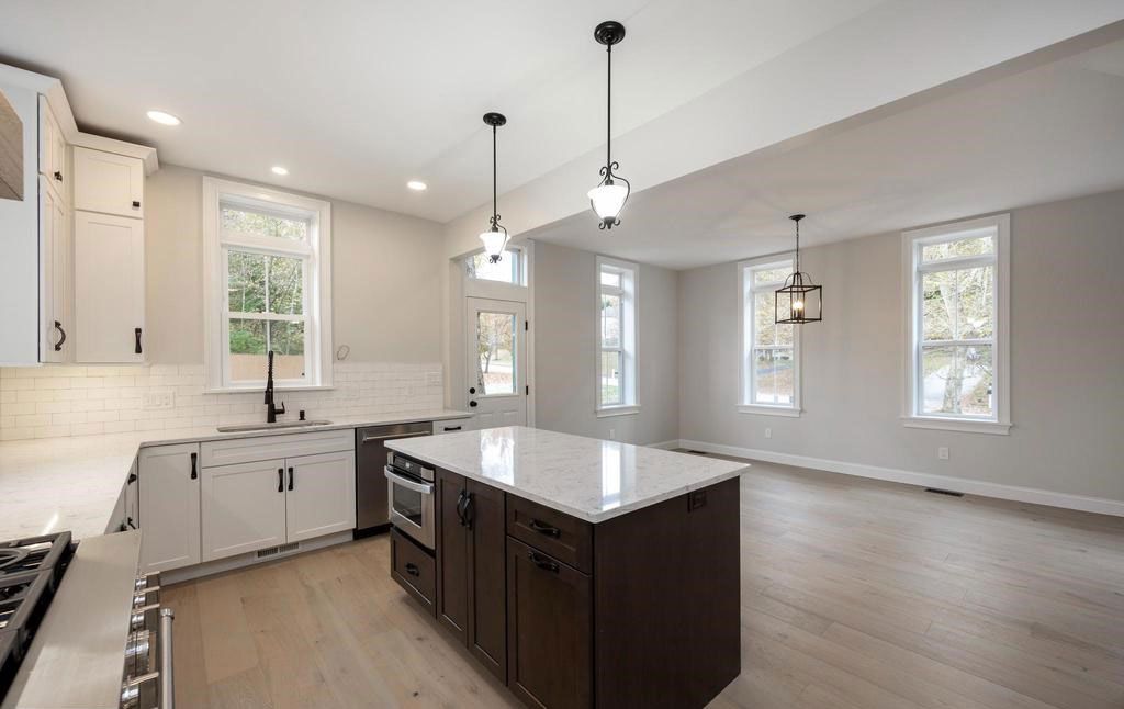 Bright modern kitchen with white cabinets, central island, pendant lights, and large windows