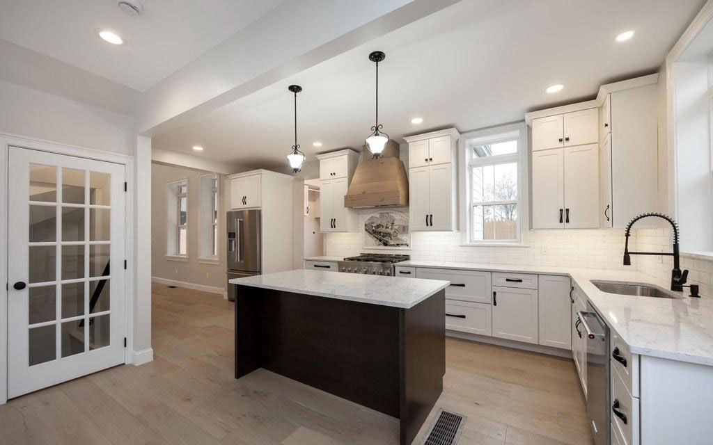 Bright modern kitchen with white cabinets, dark island, pendant lights, and hardwood floors