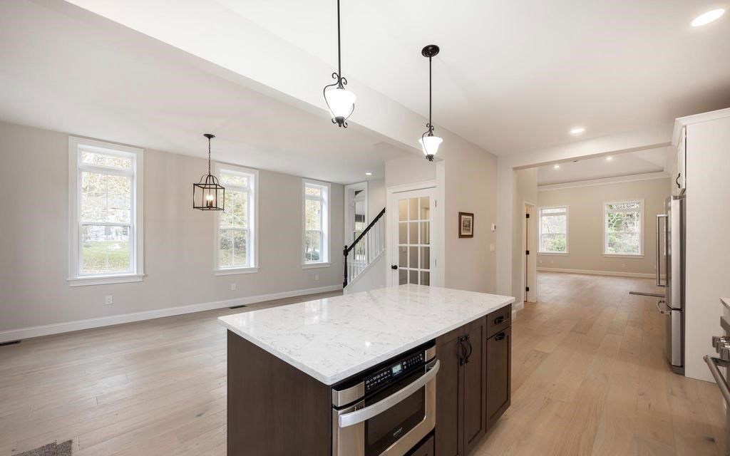 Bright open kitchen with white island, pendant lights, and light wood floors leading to a living area