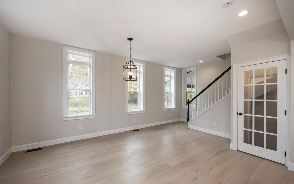 Empty living room with light wood floors, gray walls, staircase, and French doors.
